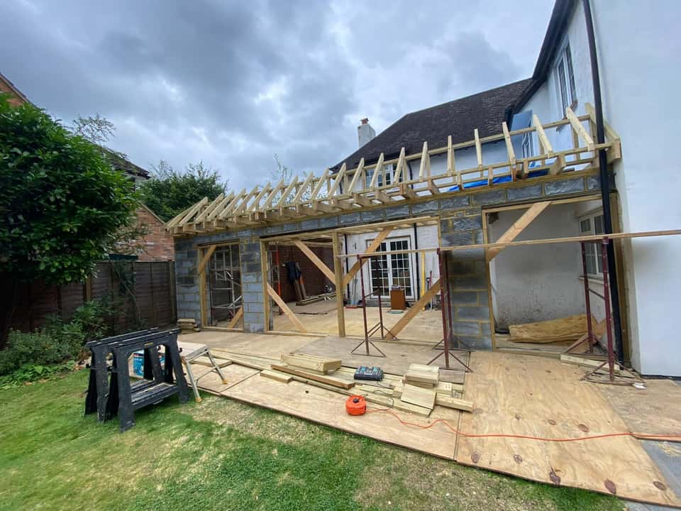 Rear house extension under construction with grey blockwork walls and a newly installed timber rafter roof frame.