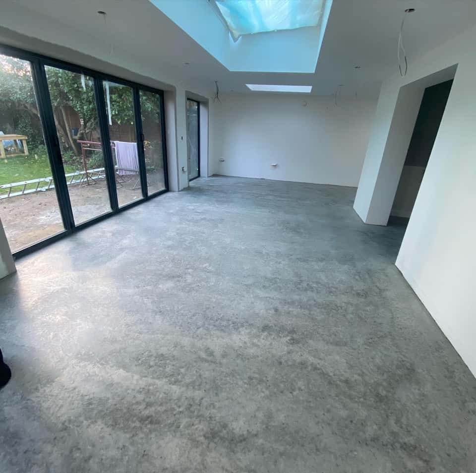 Bright house extension interior with polished grey concrete floor, white walls, skylight, and black-framed bifold doors to the garden.