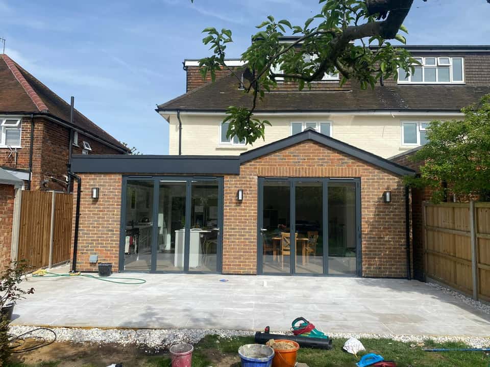 Completed brick rear extension with two sets of grey bifold doors opening onto a large light-grey porcelain patio.