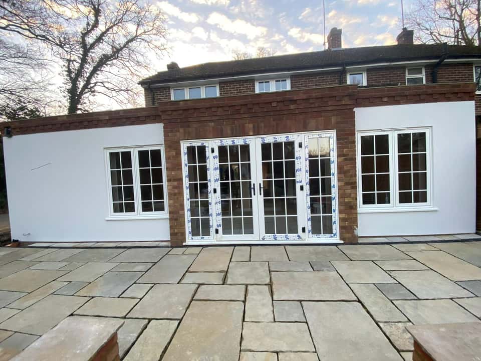 Finished single-storey rear extension with brick centre bay, rendered wings, French doors, and large stone patio.