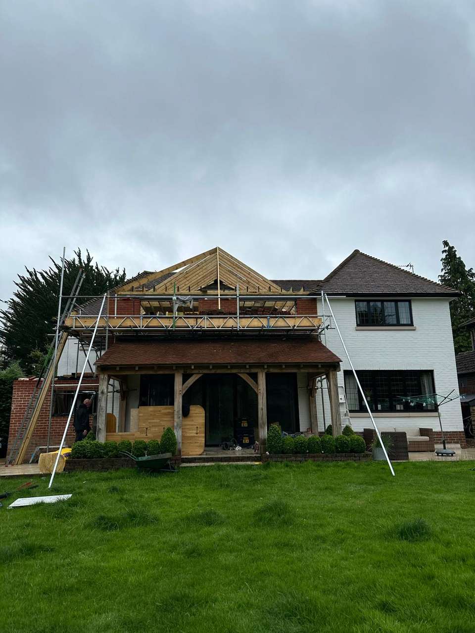 Rear house extension with oak-framed ground floor, scaffolding, and new timber gable roof structure under construction.