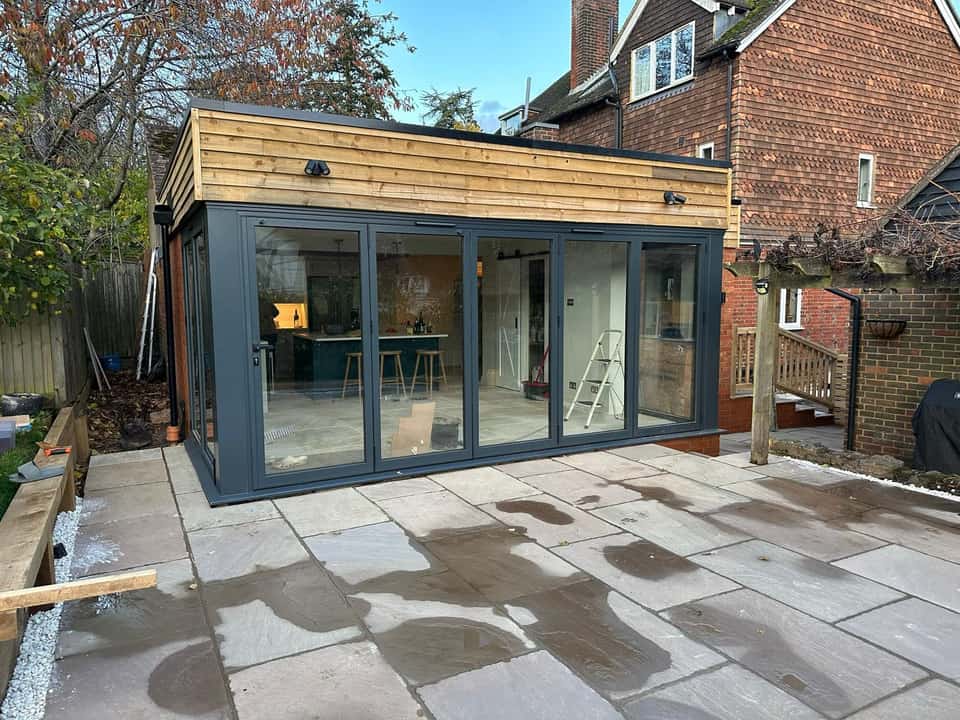 A modern rear extension with timber cladding, dark grey bi-fold doors, and a new natural stone patio.