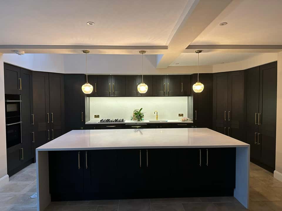 Finished modern navy kitchen with white marble waterfall island and gold pendant lights.
