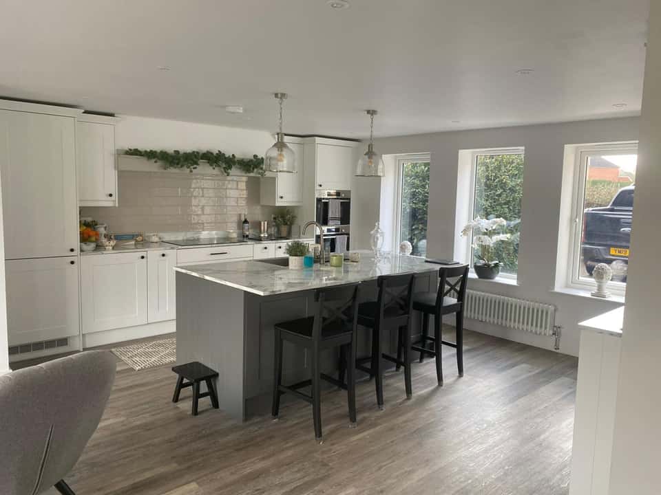 Finished modern kitchen with white and grey shaker cabinets, marble island, and pendant lights