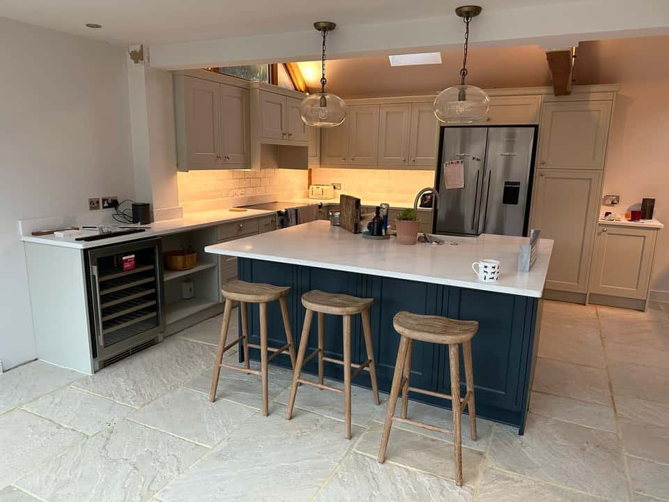 High-end kitchen with navy Shaker island, marble countertop, wooden bar stools, and globe pendant lights.
