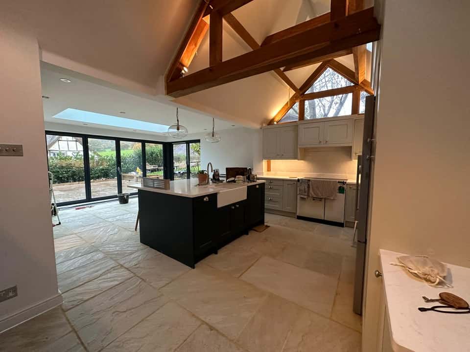 Finished vaulted kitchen extension with exposed oak trusses, dark island, and bifold doors to the patio
