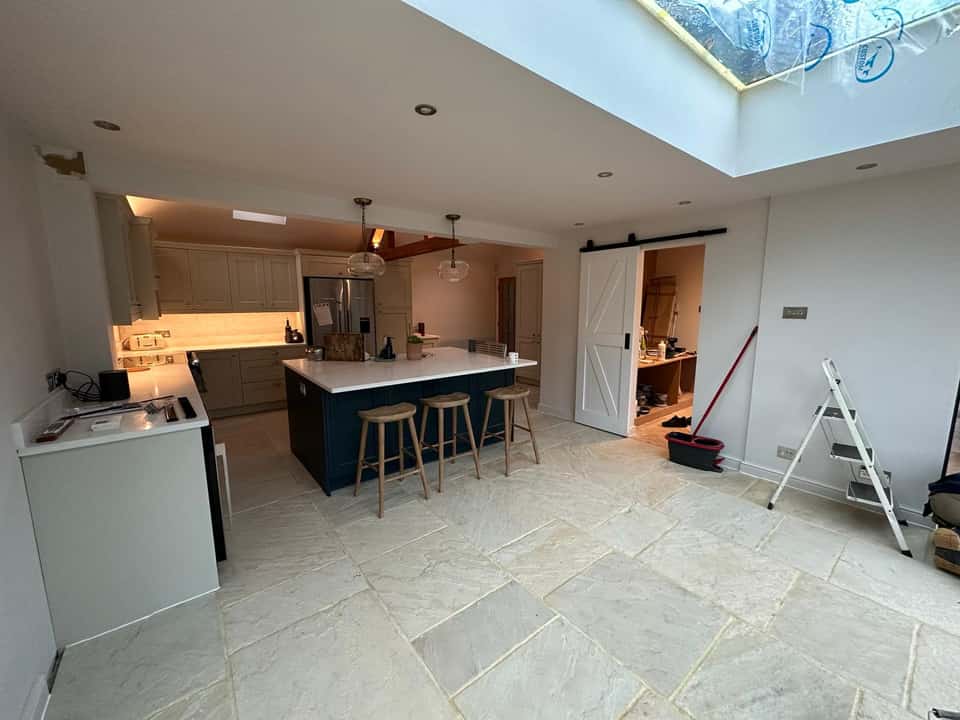 Bright modern kitchen extension with navy island, stone flooring, and large roof lantern skylight.