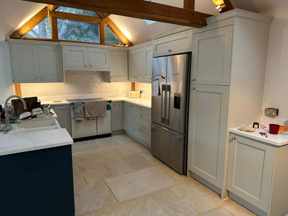 Finished sage-green Shaker kitchen with stone floor tiles, white marble countertops, and exposed timber beams on a vaulted ceiling.