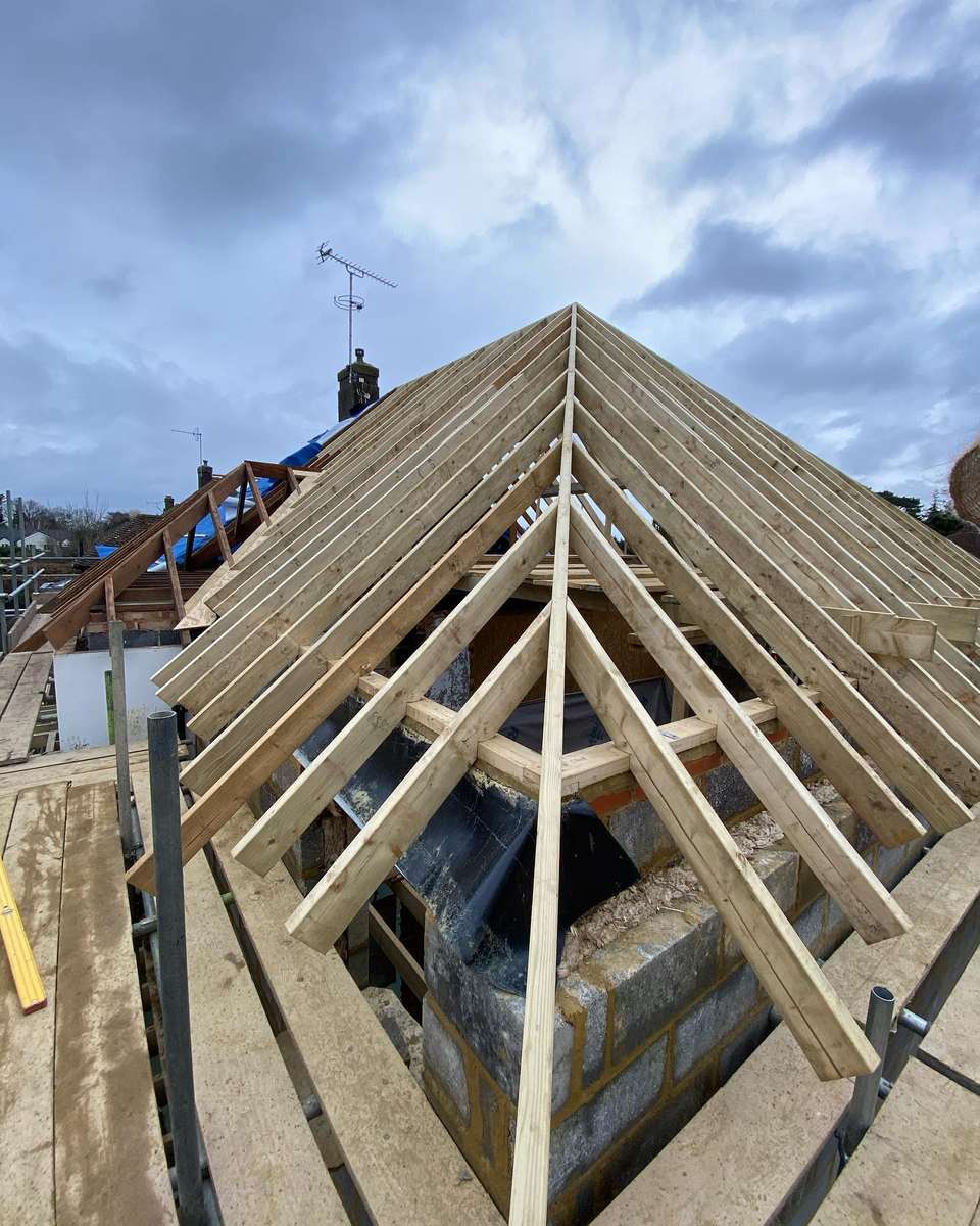 Close-up of timber roof rafters forming a multi-pitched loft conversion frame viewed from scaffolding.