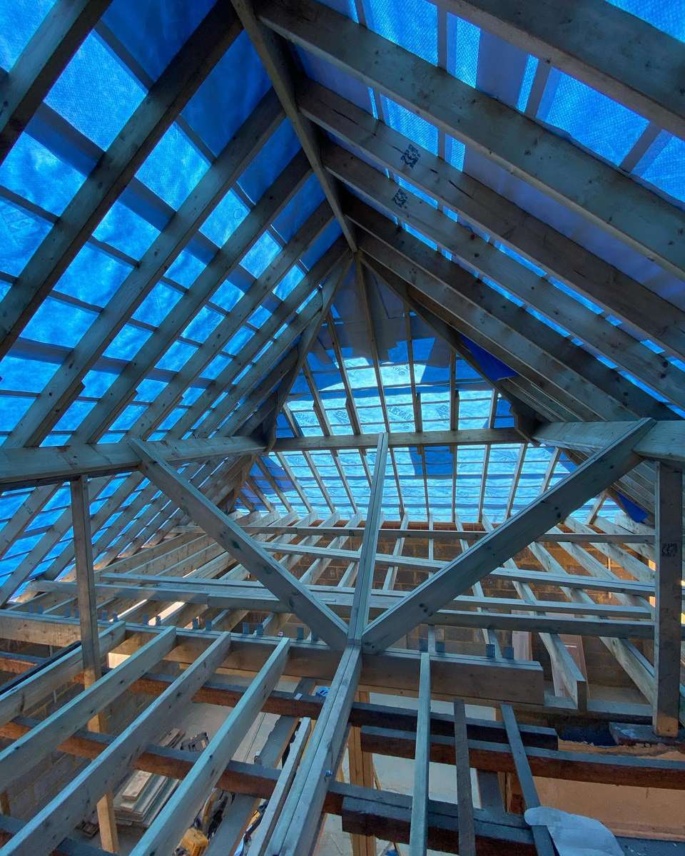 Loft conversion roof structure with timber rafters, braces, and floor joists covered by a blue waterproof membrane.