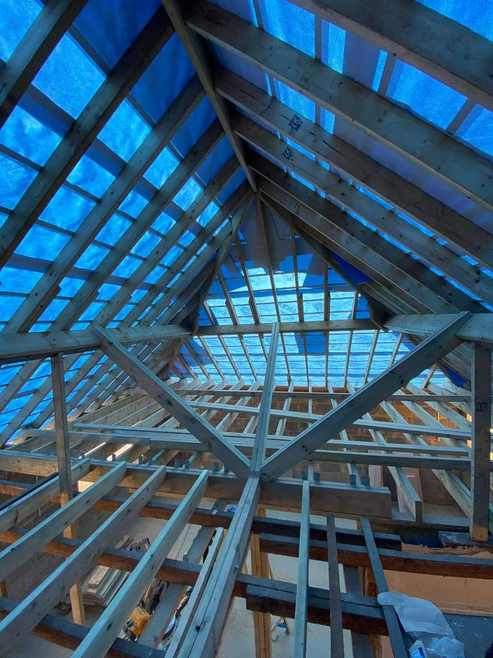 Interior view looking up at a newly built timber roof frame with rafters, joists, and diagonal bracing.