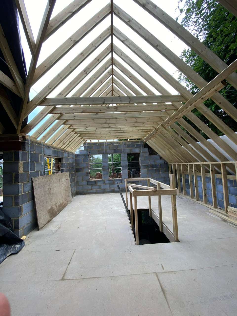 Interior loft conversion showing exposed timber roof rafters, block walls, and a temporary stairwell opening.