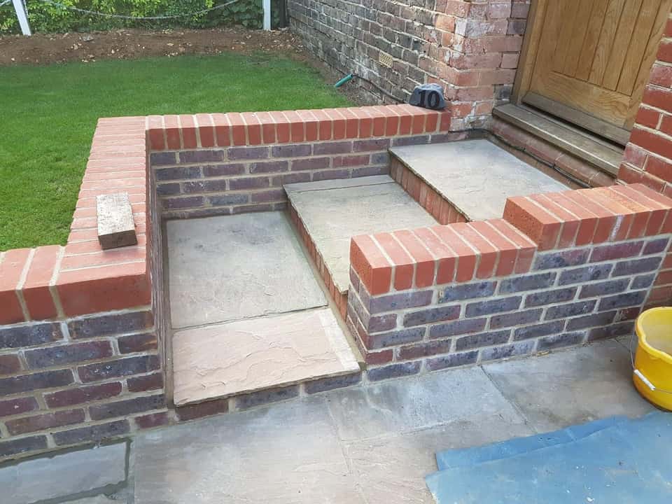 Wide natural stone entrance steps built into decorative red and dark brick retaining walls.