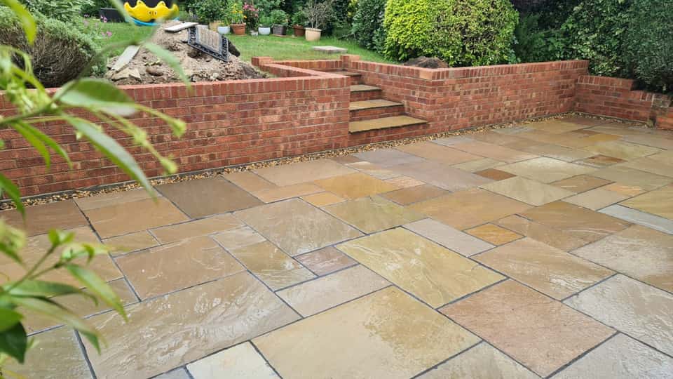 Wide view of a multi-tonal natural stone patio bordered by a red brick retaining wall with integrated stone-topped steps.