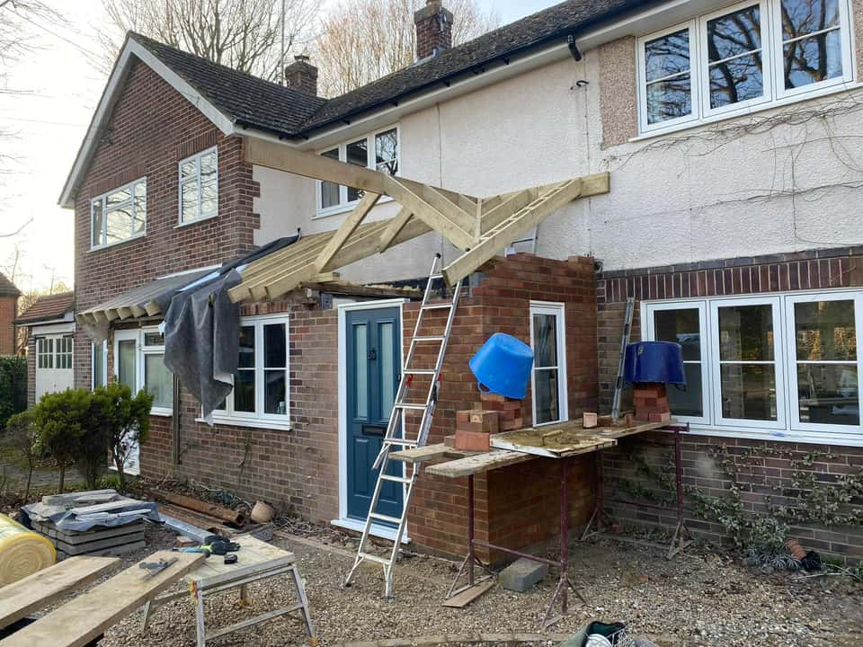 Front porch extension with new red brick walls and timber roof frame under construction.