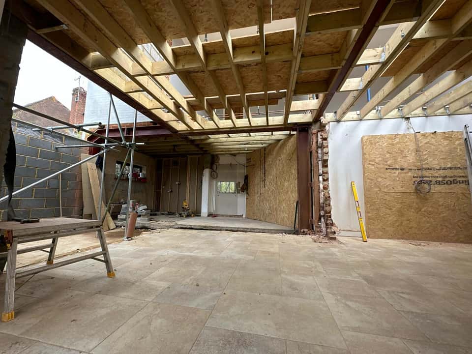 Interior open-plan space under construction with red-painted RSJ steel beams supporting new timber floor joists above.