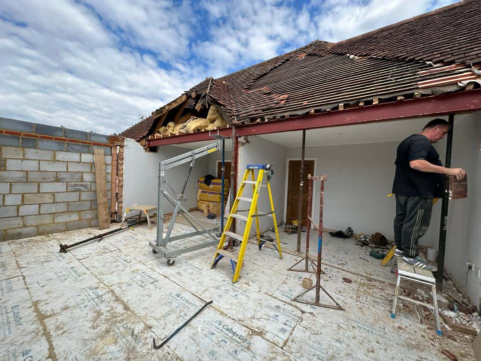 Builder working beside a large red steel RSJ beam supported by Acrow props during a structural alteration.
