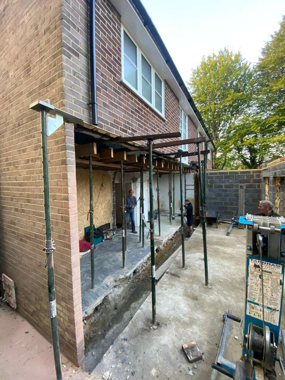 Exterior structural alteration with green acrow props supporting floor joists and a steel RSJ beam during a house extension.