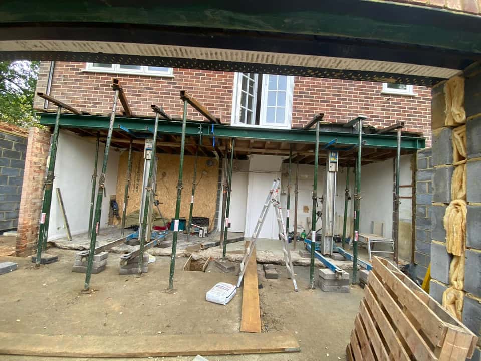 Green steel RSJ beam supported by acrow props during a rear structural opening at a brick house.