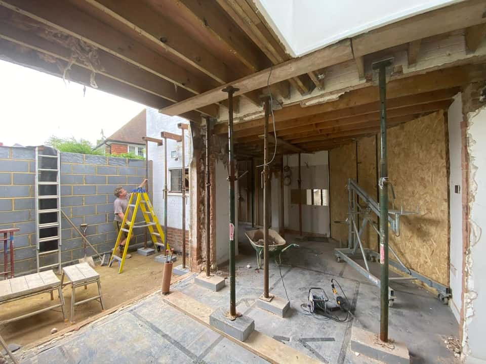 Interior renovation showing steel Acrow props supporting upper floor joists during load-bearing wall removal for an extension.