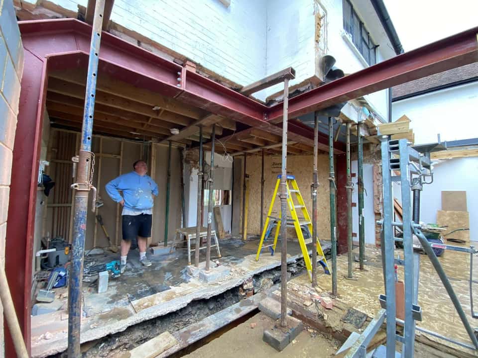 Interior structural works with large red steel RSJ beams supported by acrow props and a worker on site.