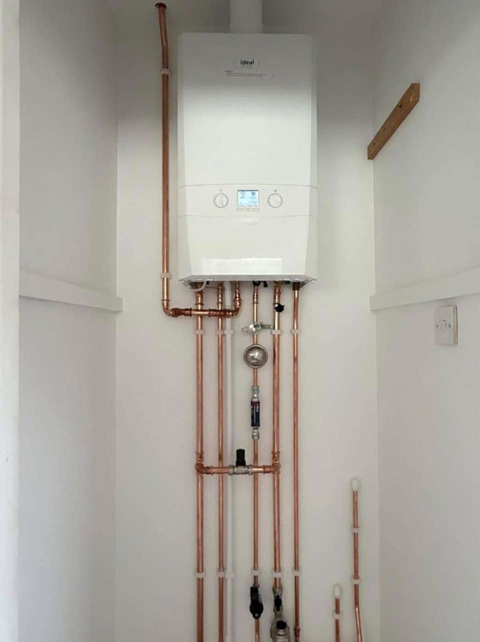 Newly installed Ideal combi boiler in a white alcove with neat vertical copper pipework