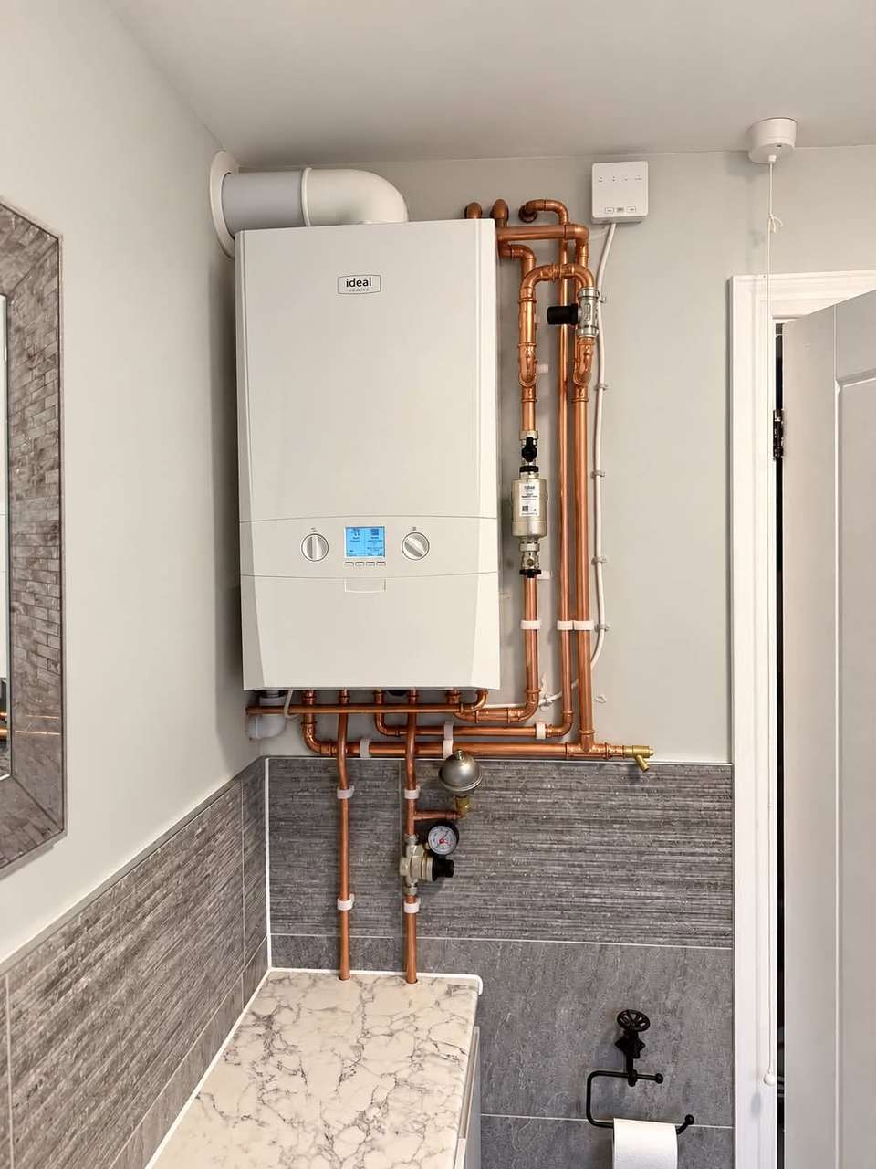 Ideal combi boiler installed in a bathroom with neatly bent copper pipework and magnetic system filter