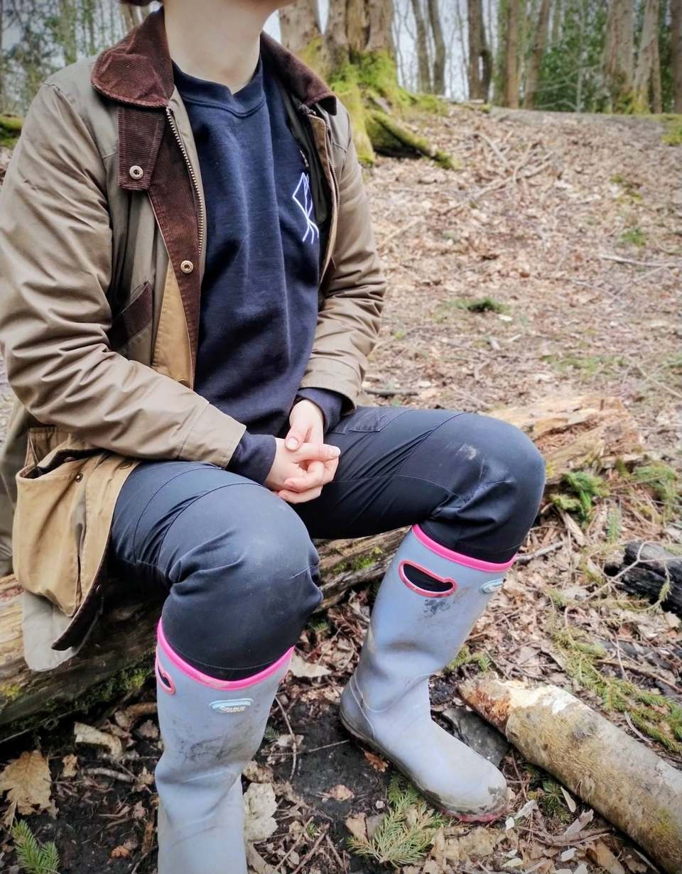 Person in a Beowulf Bushcraft sweatshirt sitting on a log in the woods