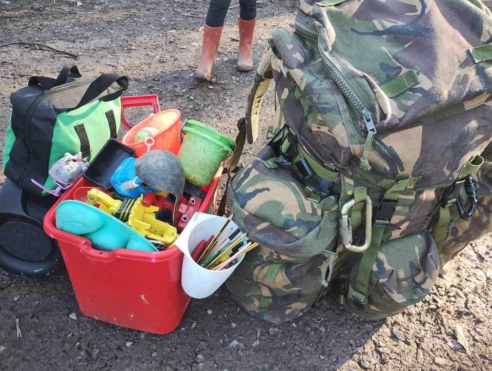 Adult rucksack beside a tray of children's outdoor toys with pink wellies in the background