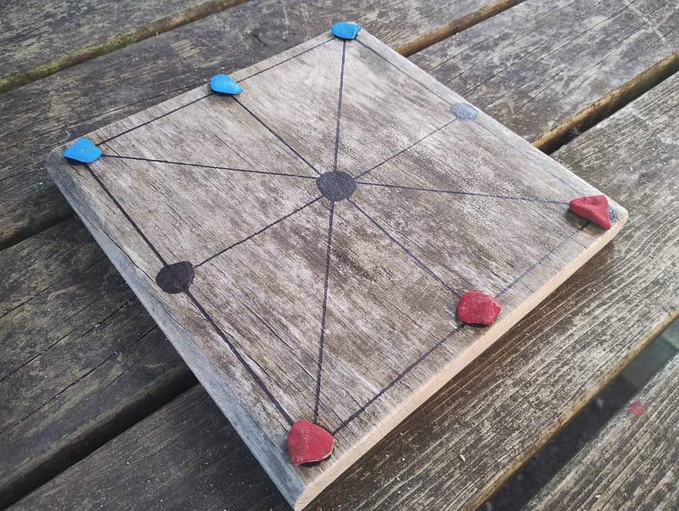 Homemade wooden board game with stone counters on a picnic table