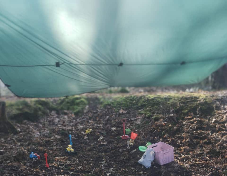 Tarp shelter and toy figures arranged on the woodland floor