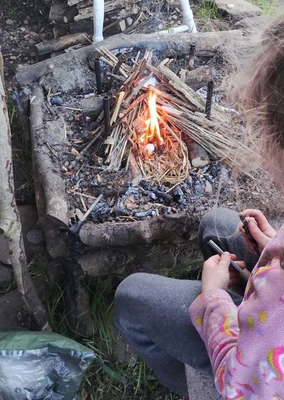 Child striking a ferro rod beside a teepee fire-lay in the woods