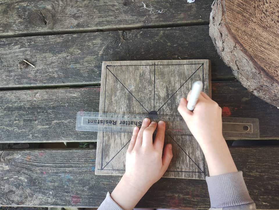 Child's hands drawing a game board on wood with chalk and a ruler