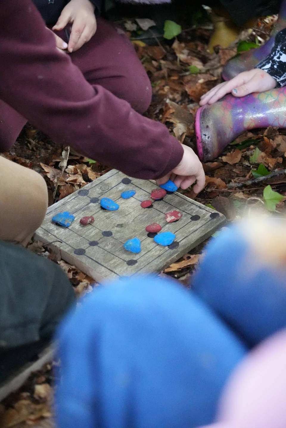 Children's hands playing a homemade wooden board game with stone counters