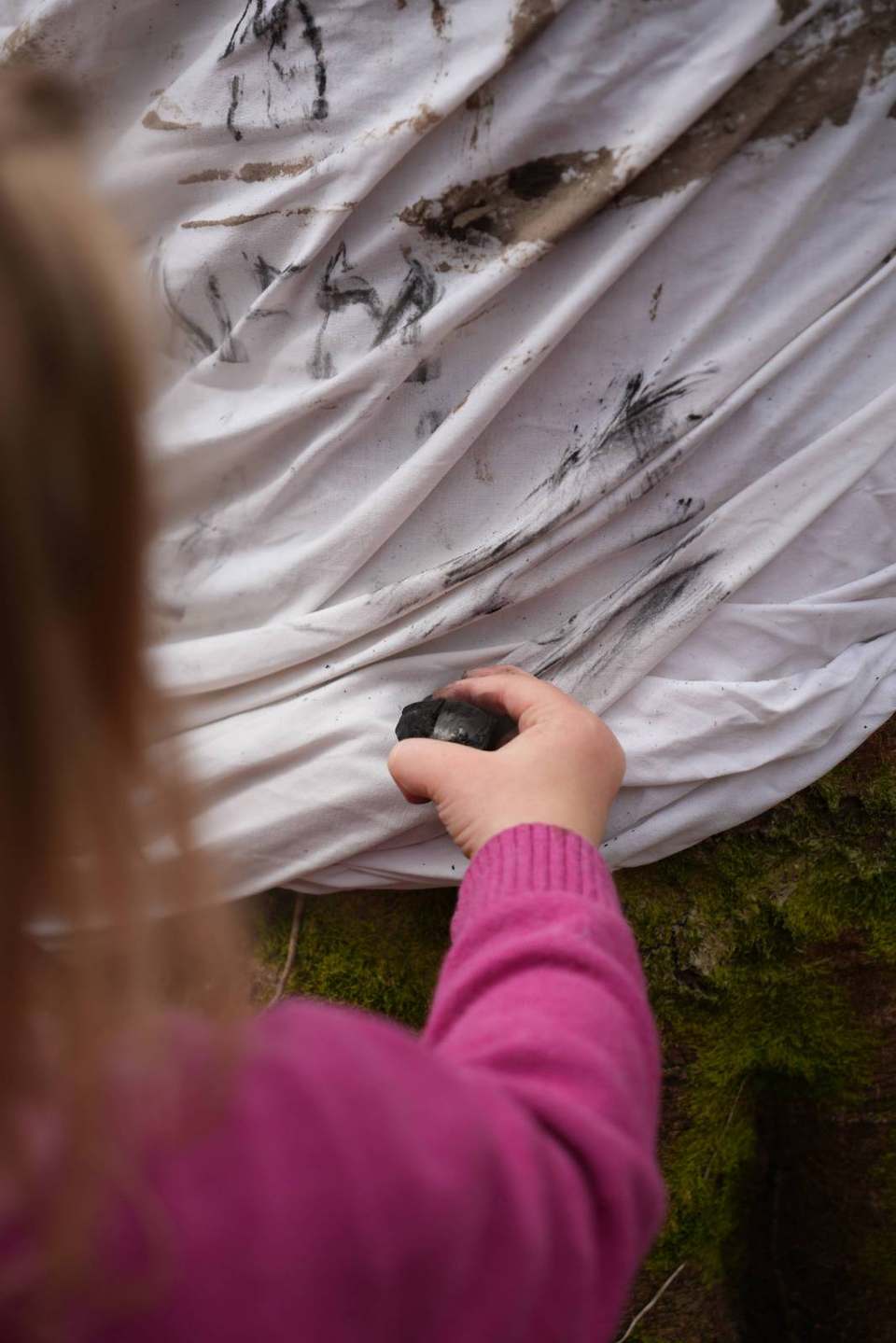 Child drawing on bark with charcoal, seen from behind