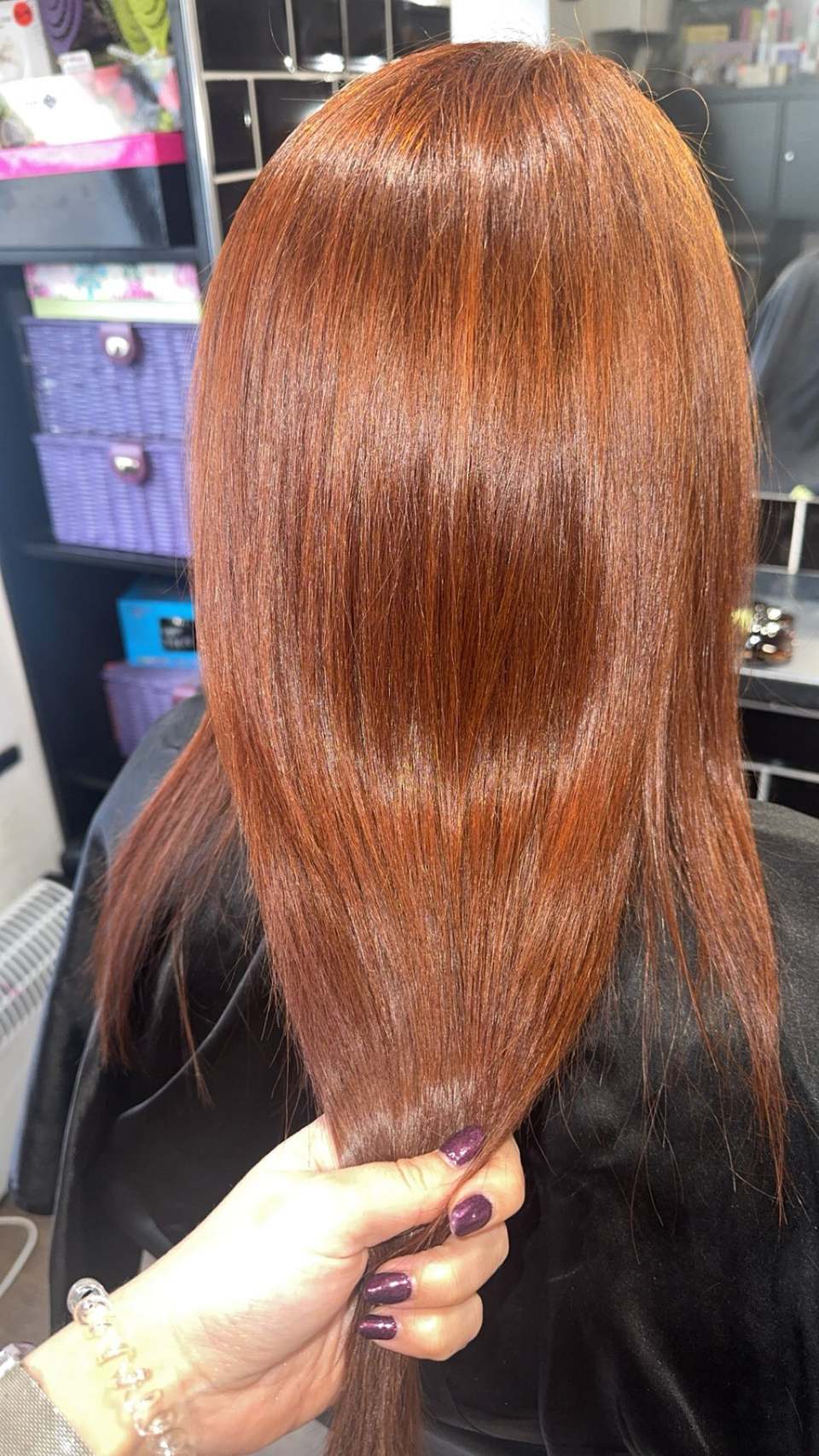 Glossy copper-red hair with high shine held in the stylist’s hand