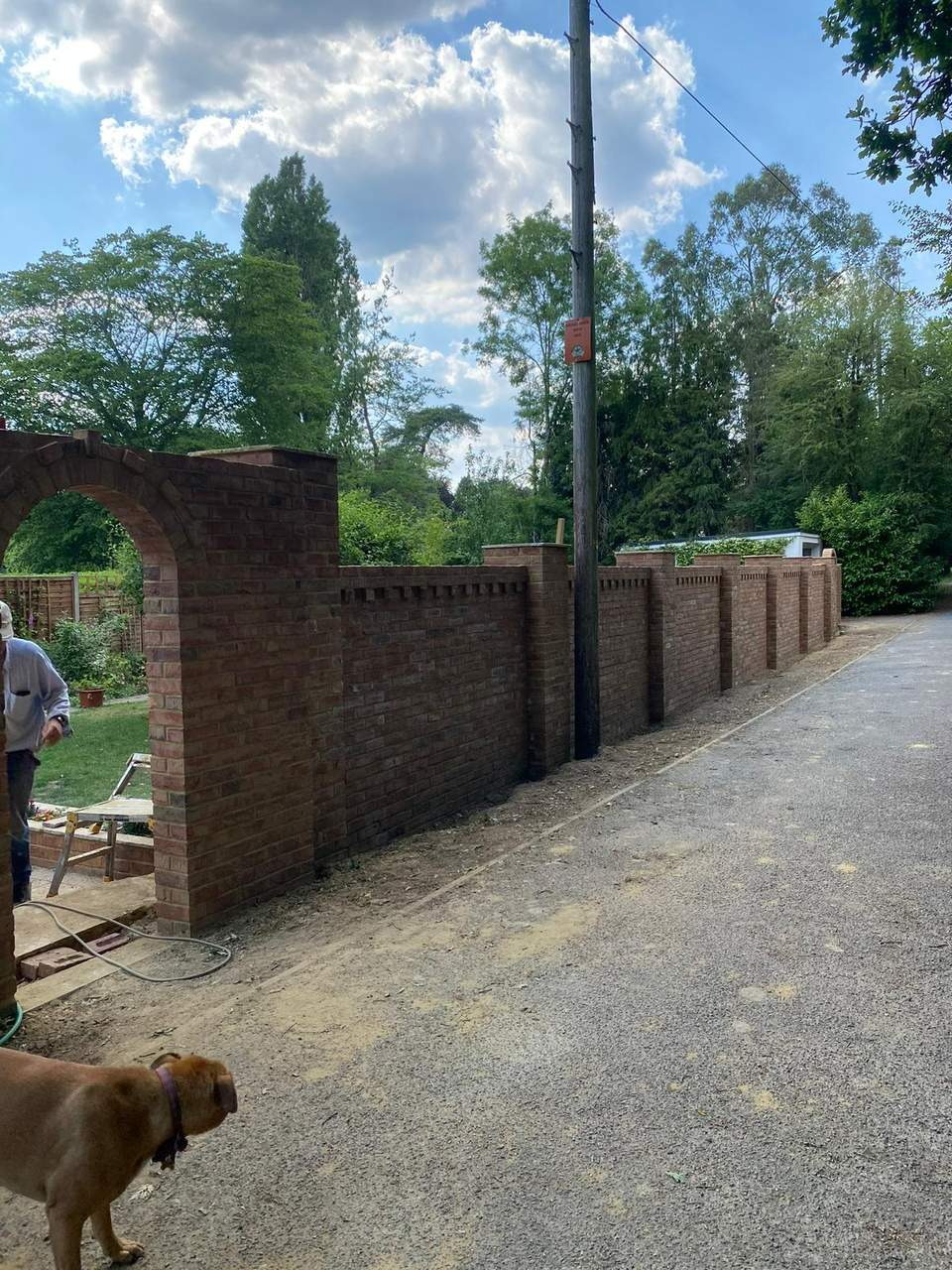 Long decorative red brick boundary wall with arched gateway and corbelled brick detailing