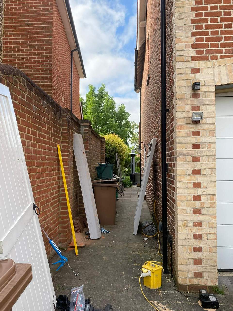White wooden gate and timber posts being installed in a paved side passage between brick walls.