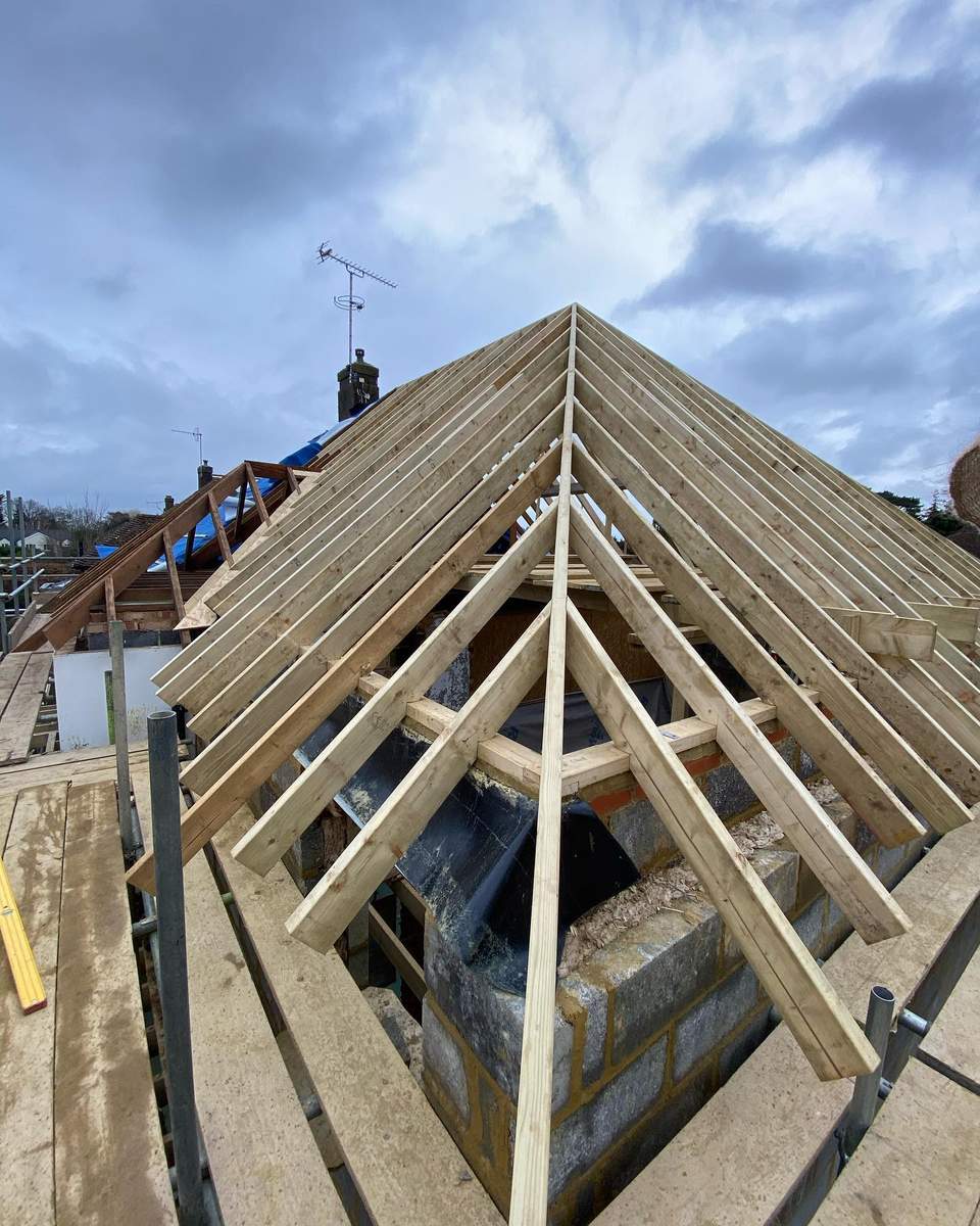 Close-up of timber roof rafters forming a multi-pitched loft conversion frame viewed from scaffolding.