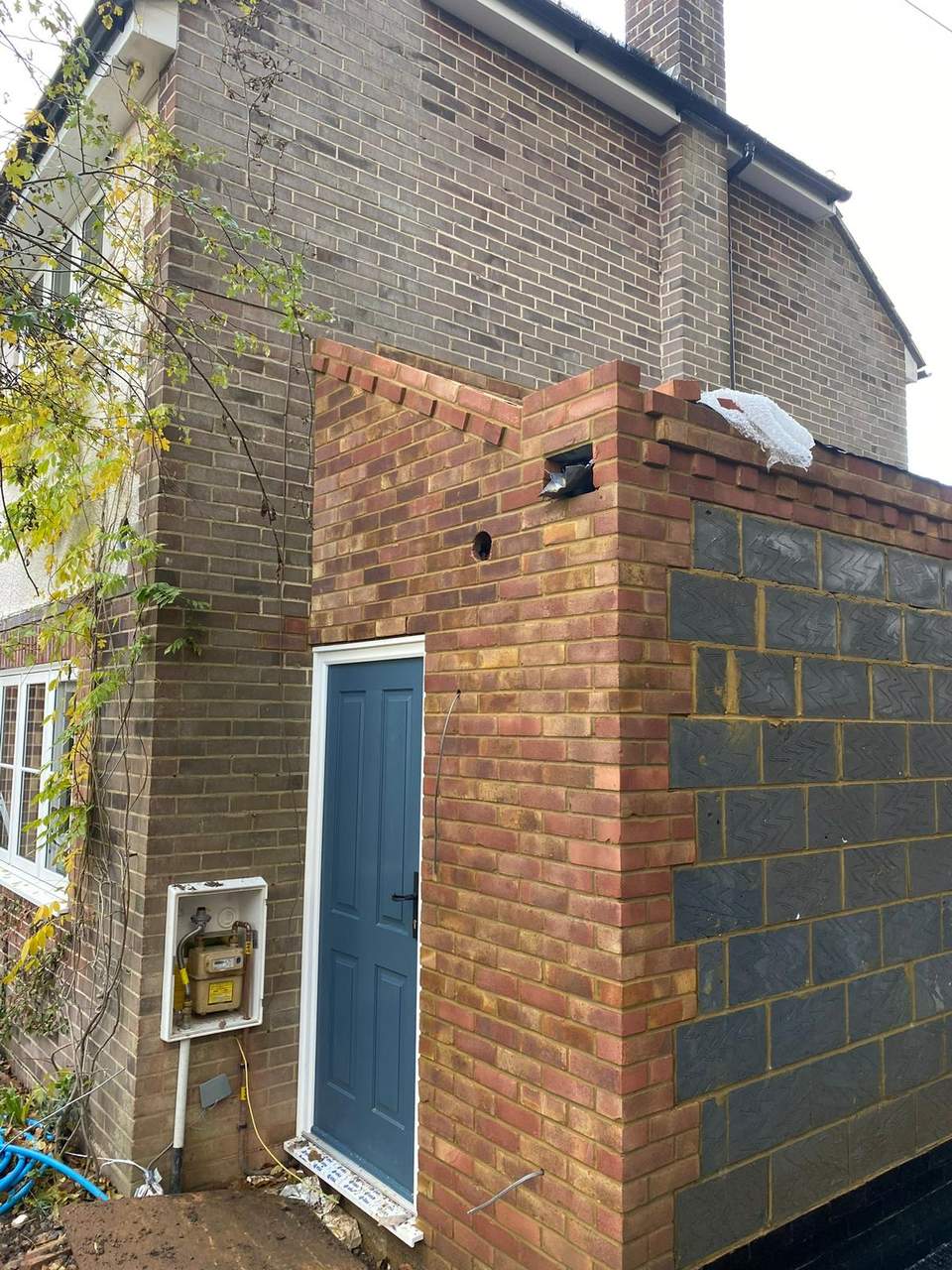 Small brick porch under construction with a blue panelled door installed against an existing brick house.