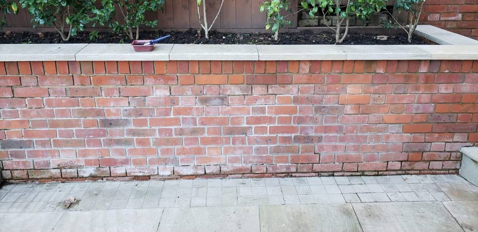 Garden brick wall with stone coping and a dirty grey patio before pressure washing