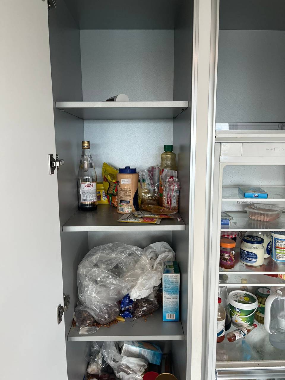 Larder cupboard full of food beside a stocked fridge before clearing
