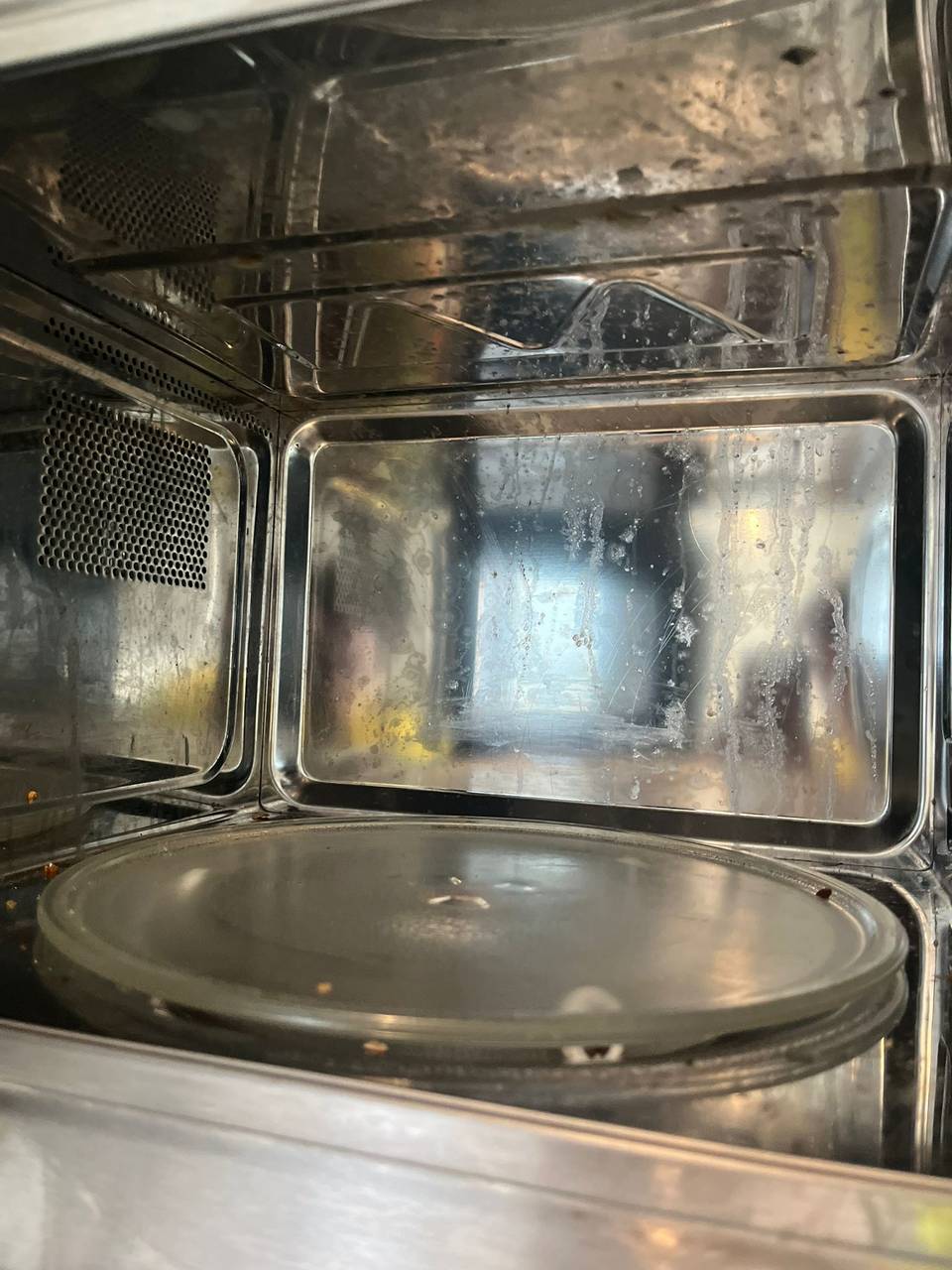 Grimy stainless steel microwave interior with grease spots before cleaning