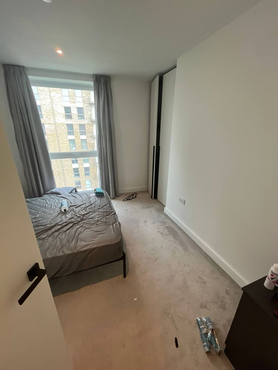 Tidy bedroom with a made bed and cleaning bottles beside a large window after clearing
