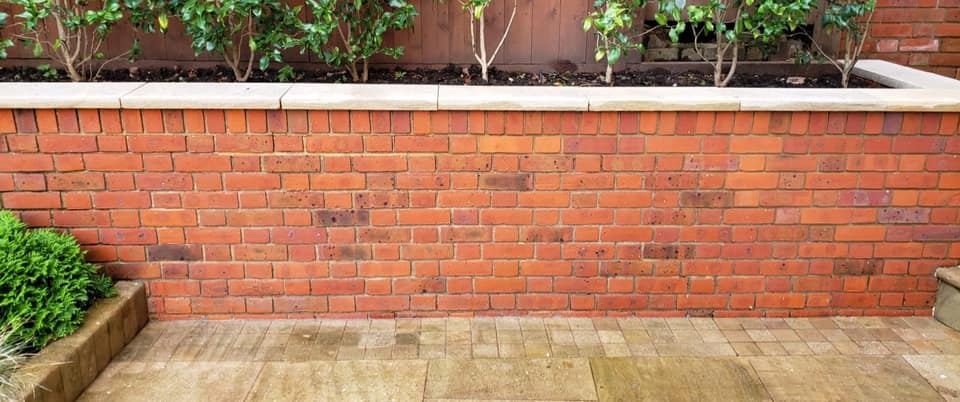 Bright red brick garden wall and clean stone patio after pressure washing