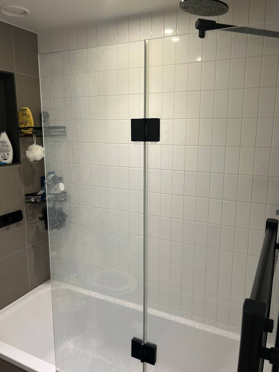 Clean white-tiled shower over bath with a spotless glass screen after cleaning