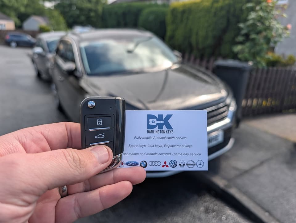 Hand holding a newly cut Volkswagen car key with a Darlington Keys business card outside a home