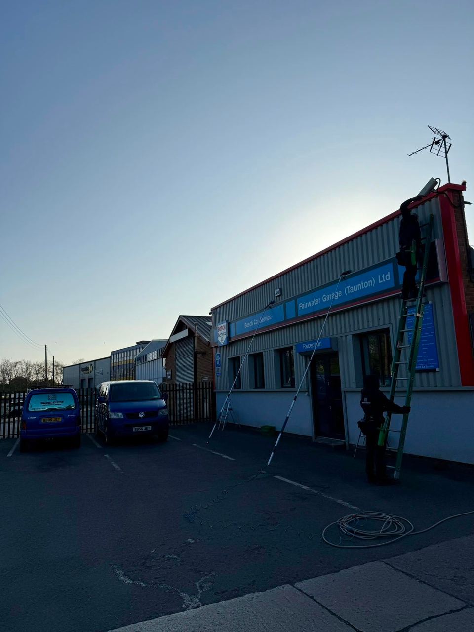 Cleaner using a reach pole to work at gutter height on a building at dusk