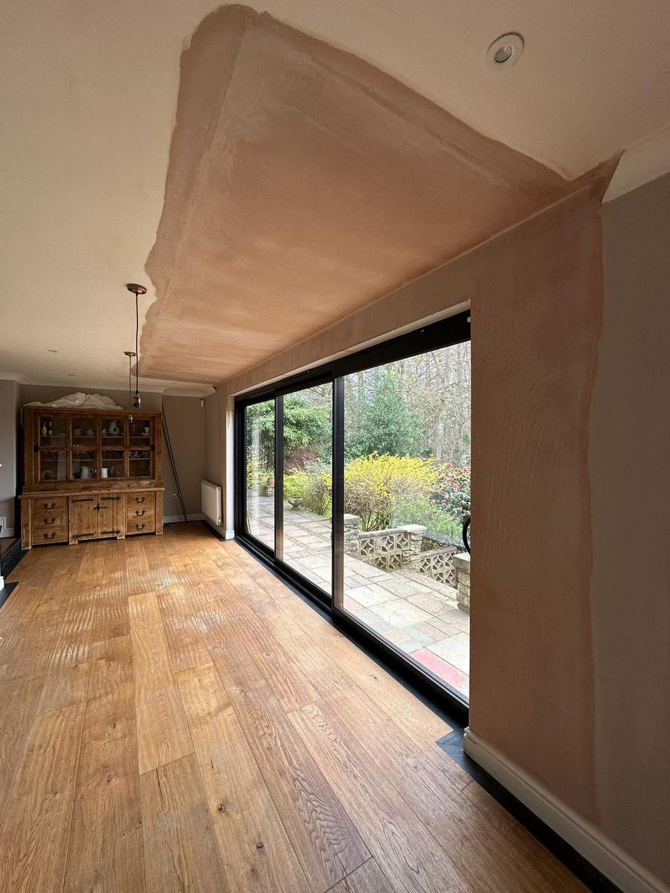 Interior room with fresh plaster around new black-framed sliding glass doors overlooking a garden patio