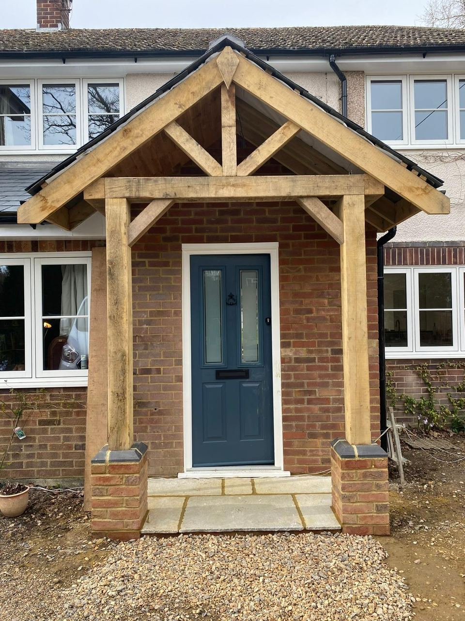 New oak timber porch with king-post truss, brick plinths, and a dark blue front door.